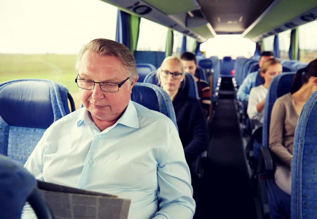 man-reading-newspaper-in-a-full-tour-bus